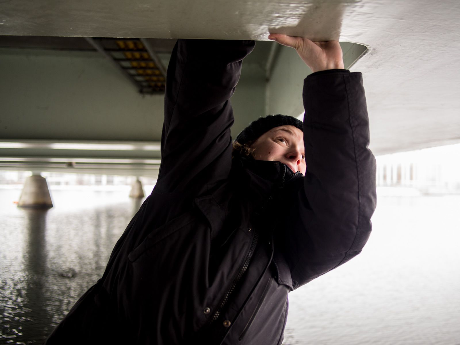 Josefine sträcker sig efter något på underredet på en bro.