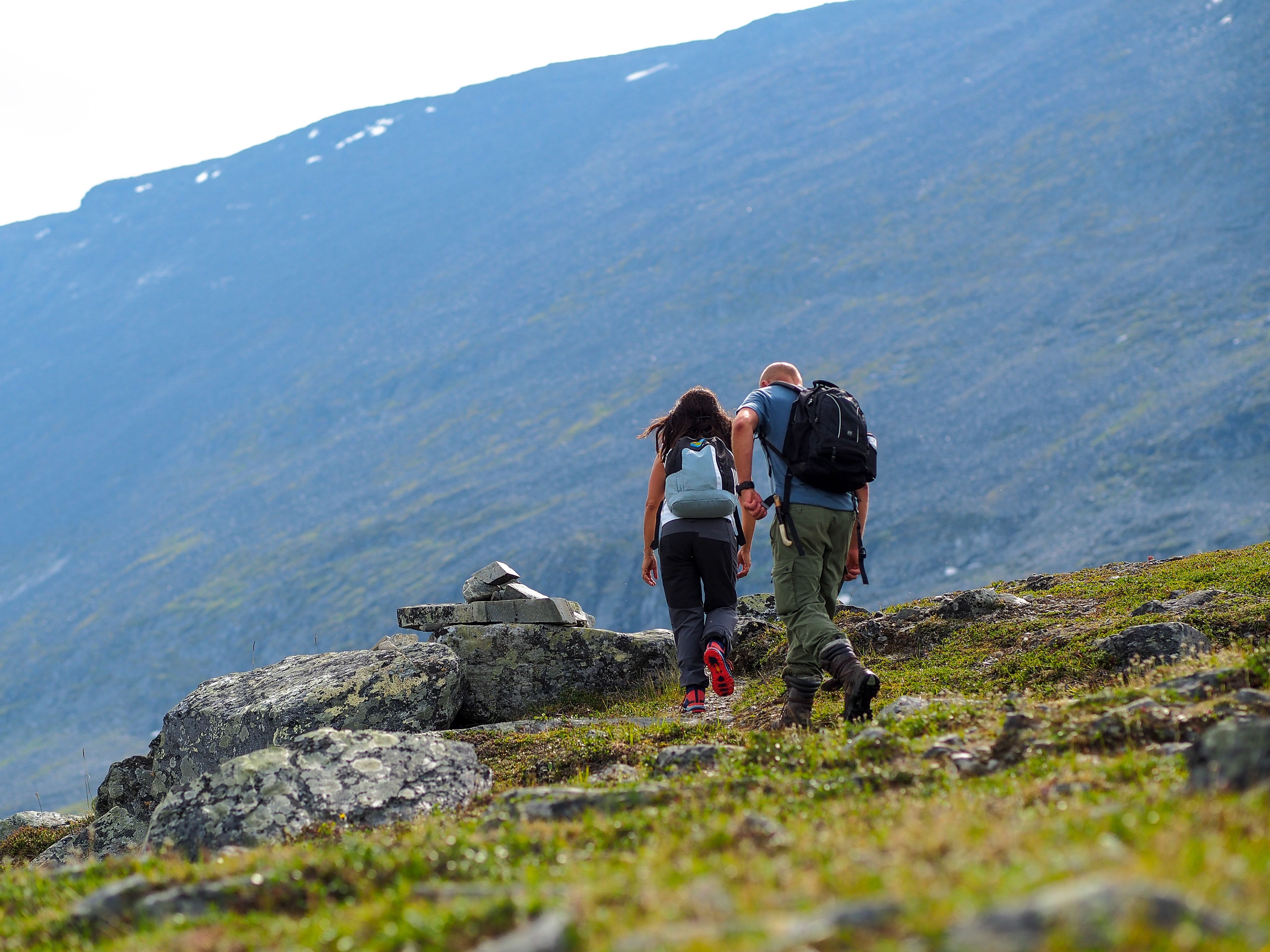 Två personer med ryggsäckar som går upp mot ett stenrösa med kalfjäll i bakgrunden