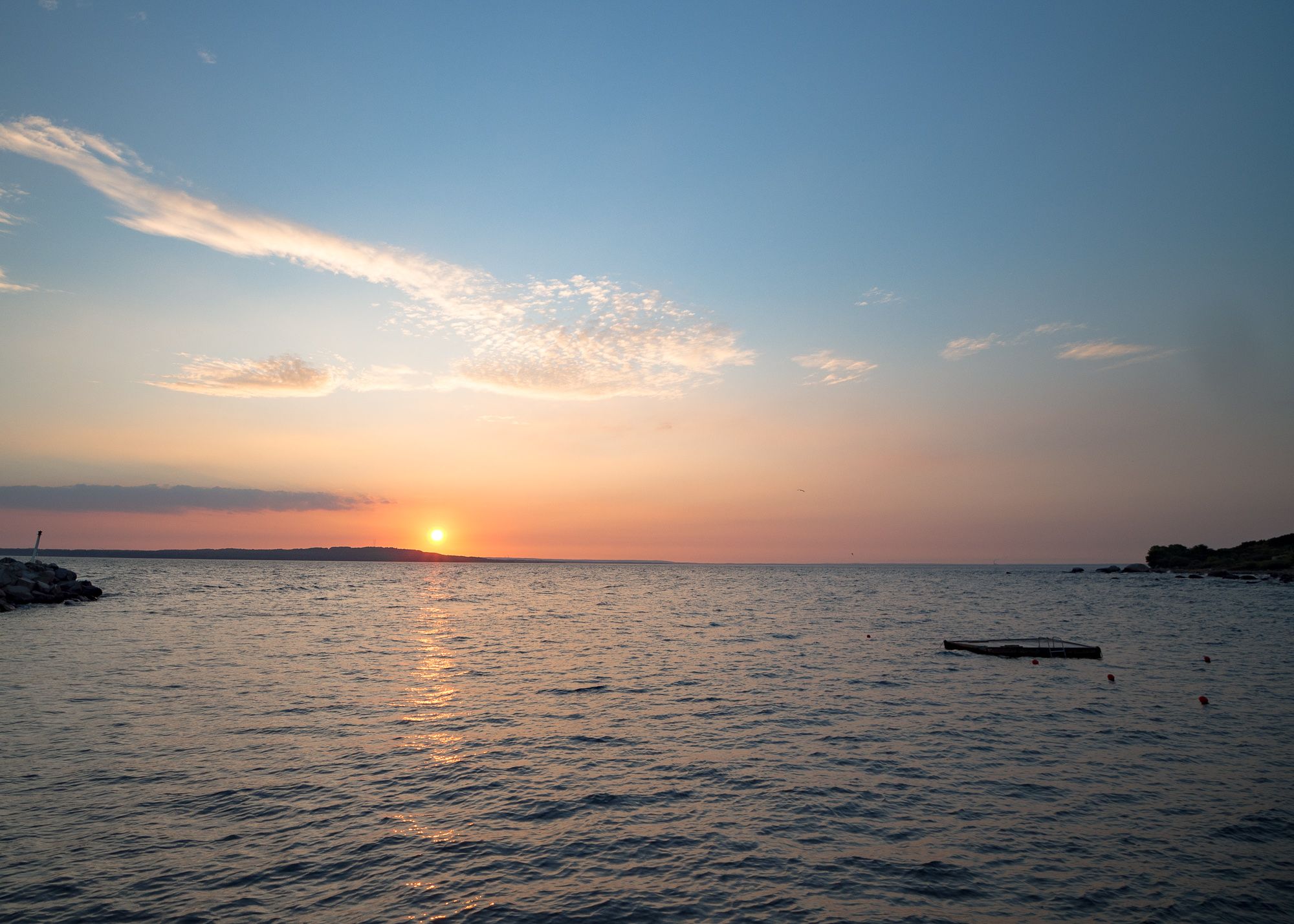 En solnedgång över havet. Vågorna krusar sig lite och ger in inperfekt reflektion av solen.