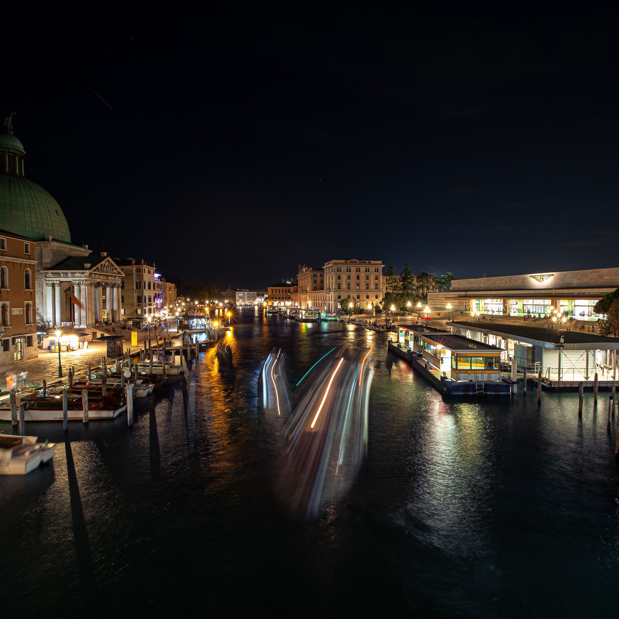 Canal Grande intill huvudstationen på natten. Ljuset från båtarna bildar långa sträck från den långa exponeringen