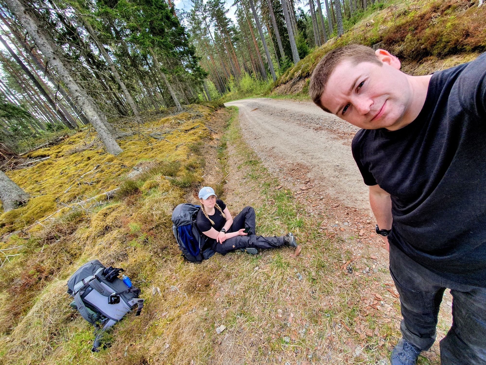 En selfie med Josefine i bakgrunden sittandes. Det ligger en ryggsäck på marken.