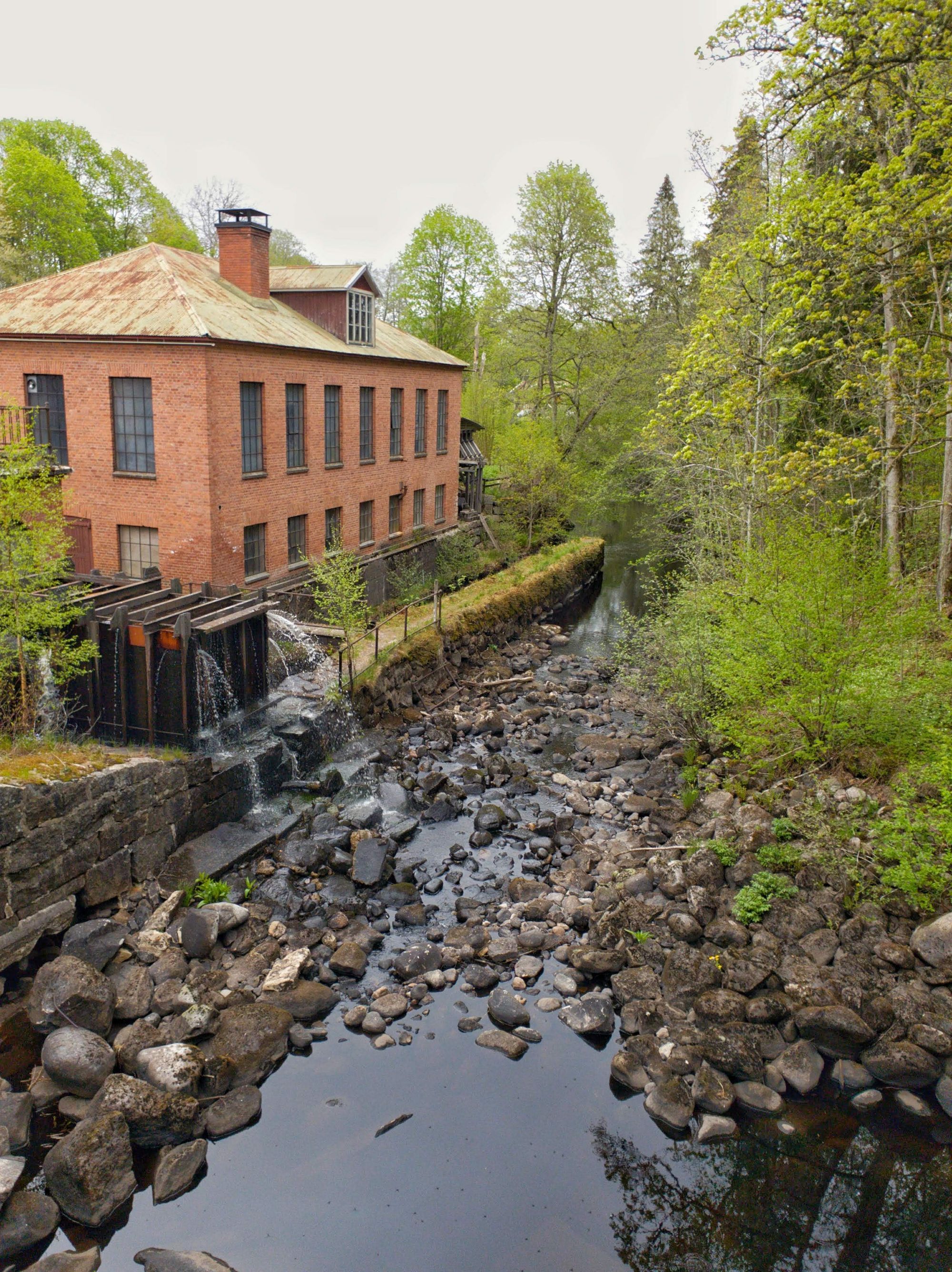 En nästan torrlagd flod intill en gammal industrilokal byggd i tegel.