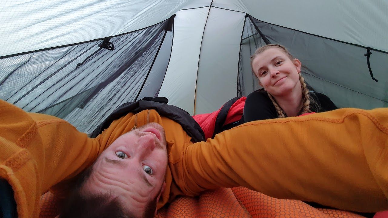 En selfie i ett tält där jag (Gustav) ligger upp och ner och håller kameran, Josefine är snett bakom och tittar in i kameran.