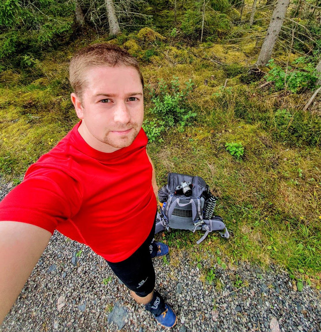 Selfie på Gustav i röd tröja tagen uppifrån. På marken ligger en ryggsäck.