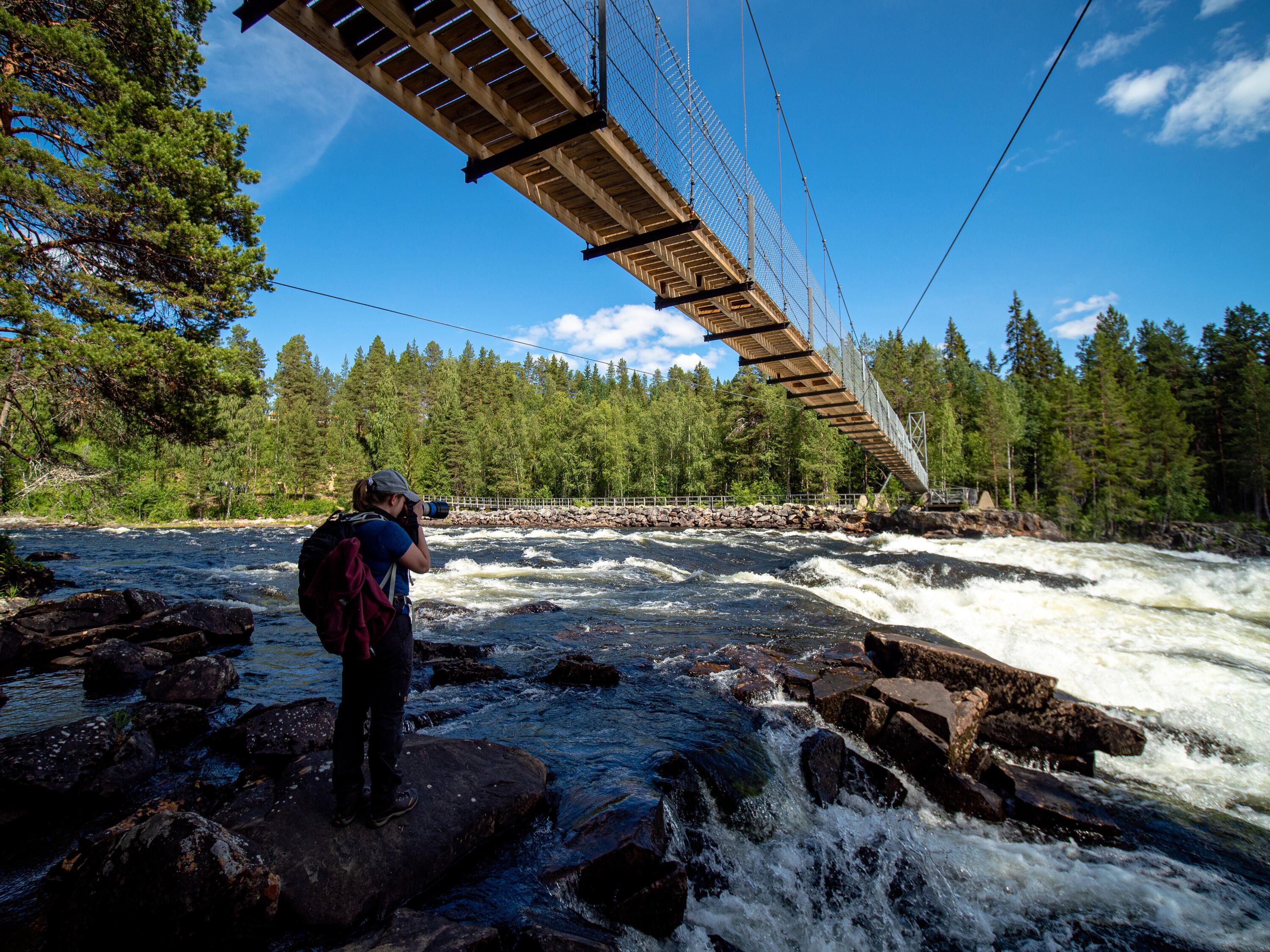 En person med en kamera i handen som står under en bro som går över en fors