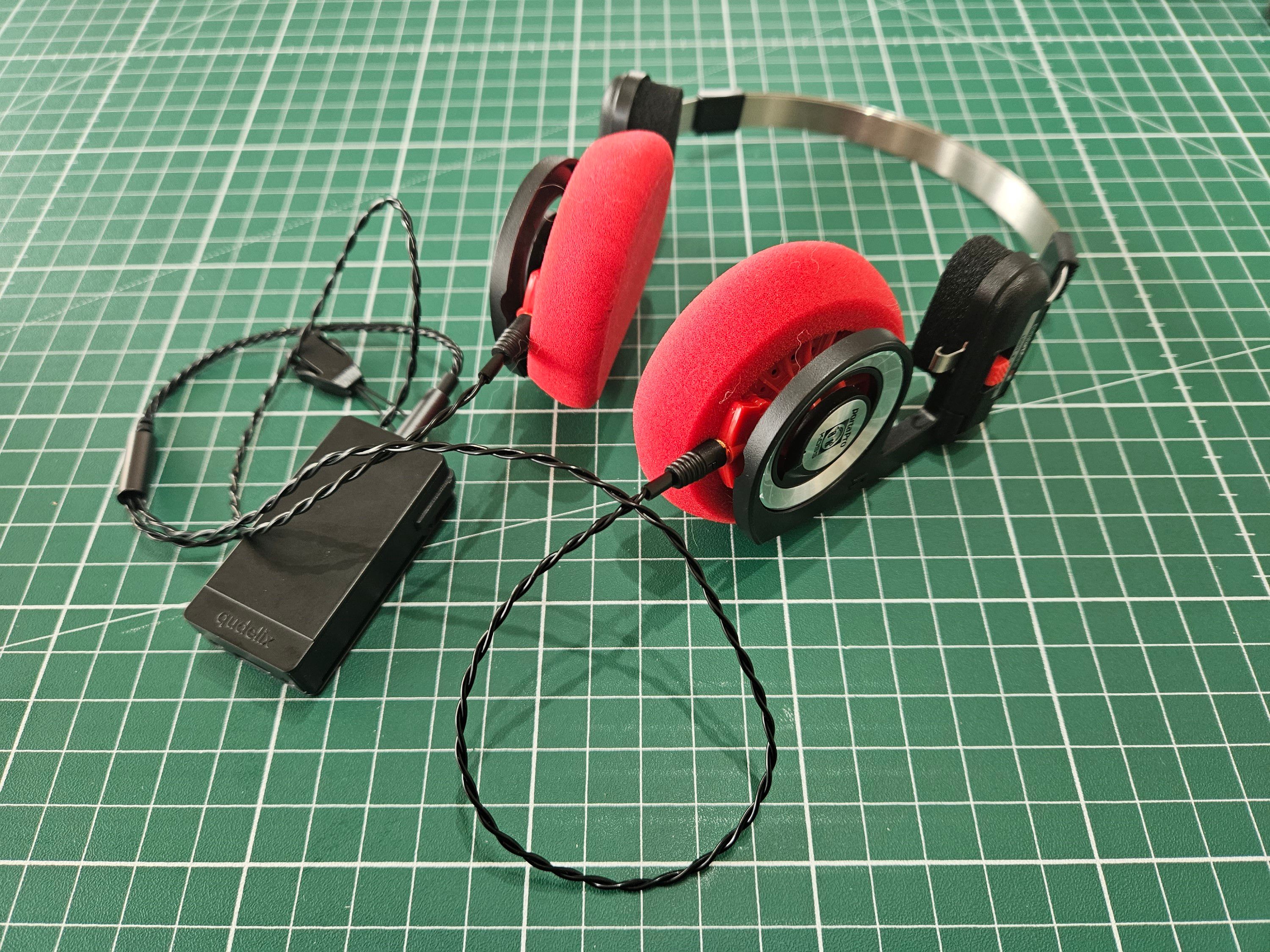 Ett par Koss Porta Pro med röda Yaxikuddar, en kort flätad kabel som sitter i en svart blåtandsdongel.