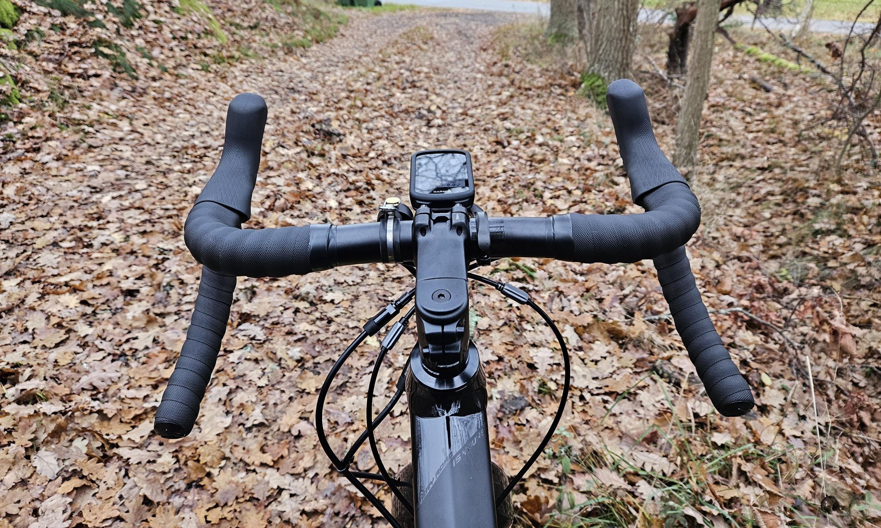 Styret på en svart gruscykel. Styret är av typen bockstyre och har en cykeldator monterad på ett fäste som sticker ut lite framför styret.