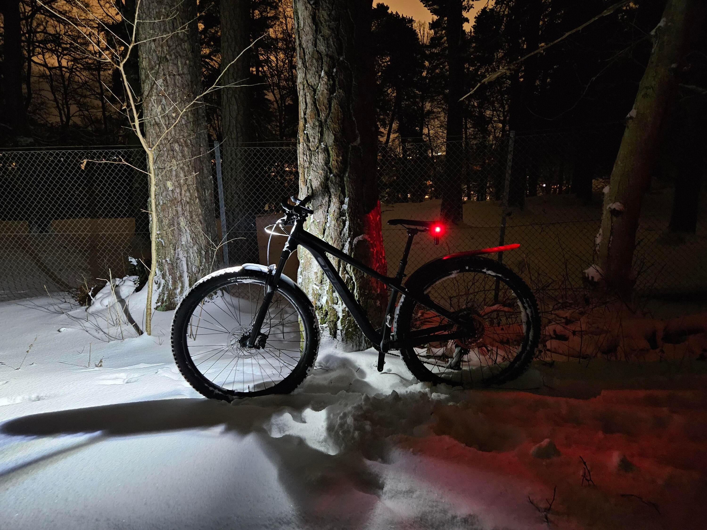 En stigcykel sedd i profil som lutar mot ett träd mitt i natten. Cykeln har lampor som lyser med kraftigt vitt sken fram och rött bak
