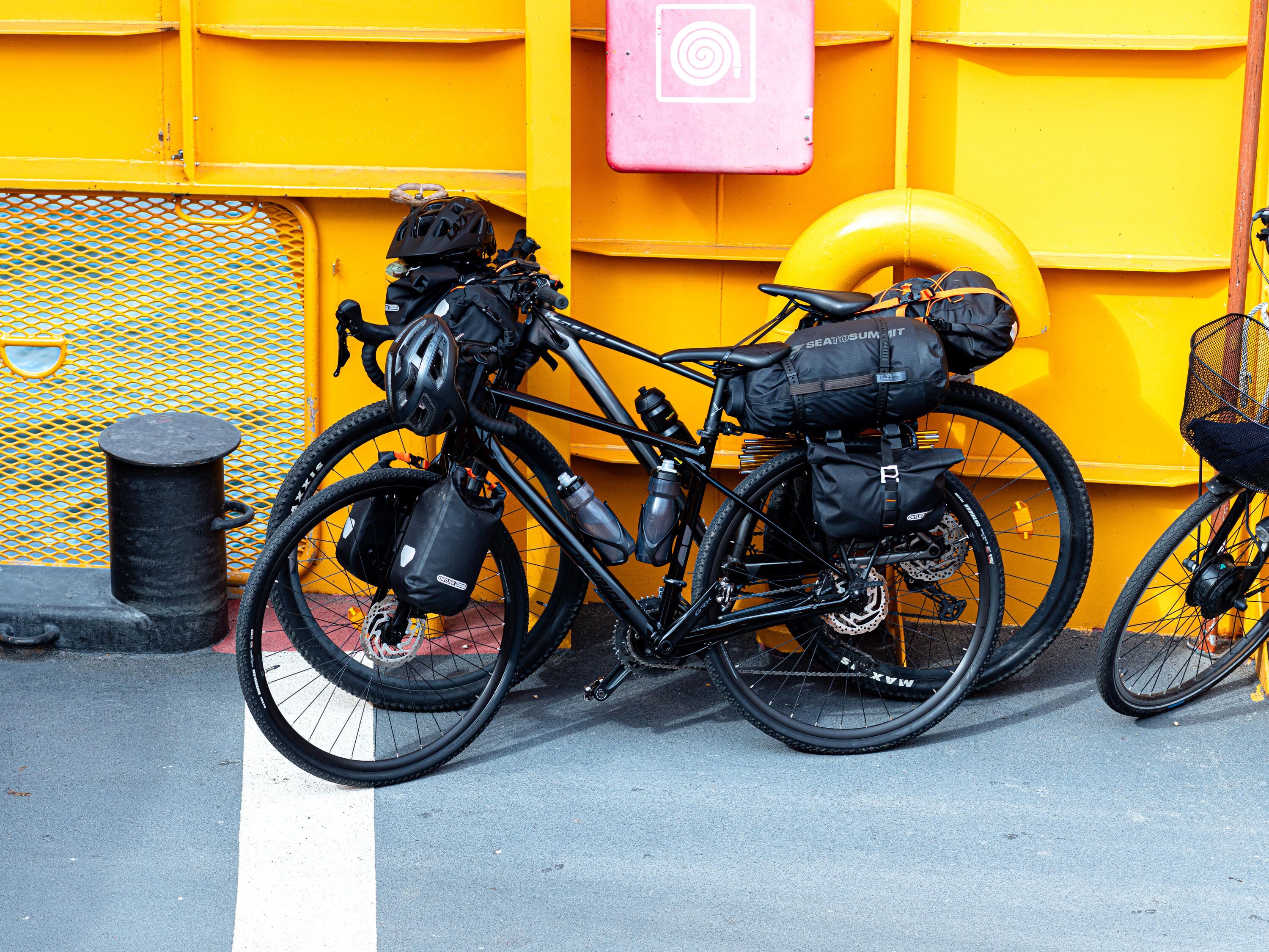 Två cyklar som står lutade mot sidan på en gul färja. Cyklarna är fullastade med väskor.