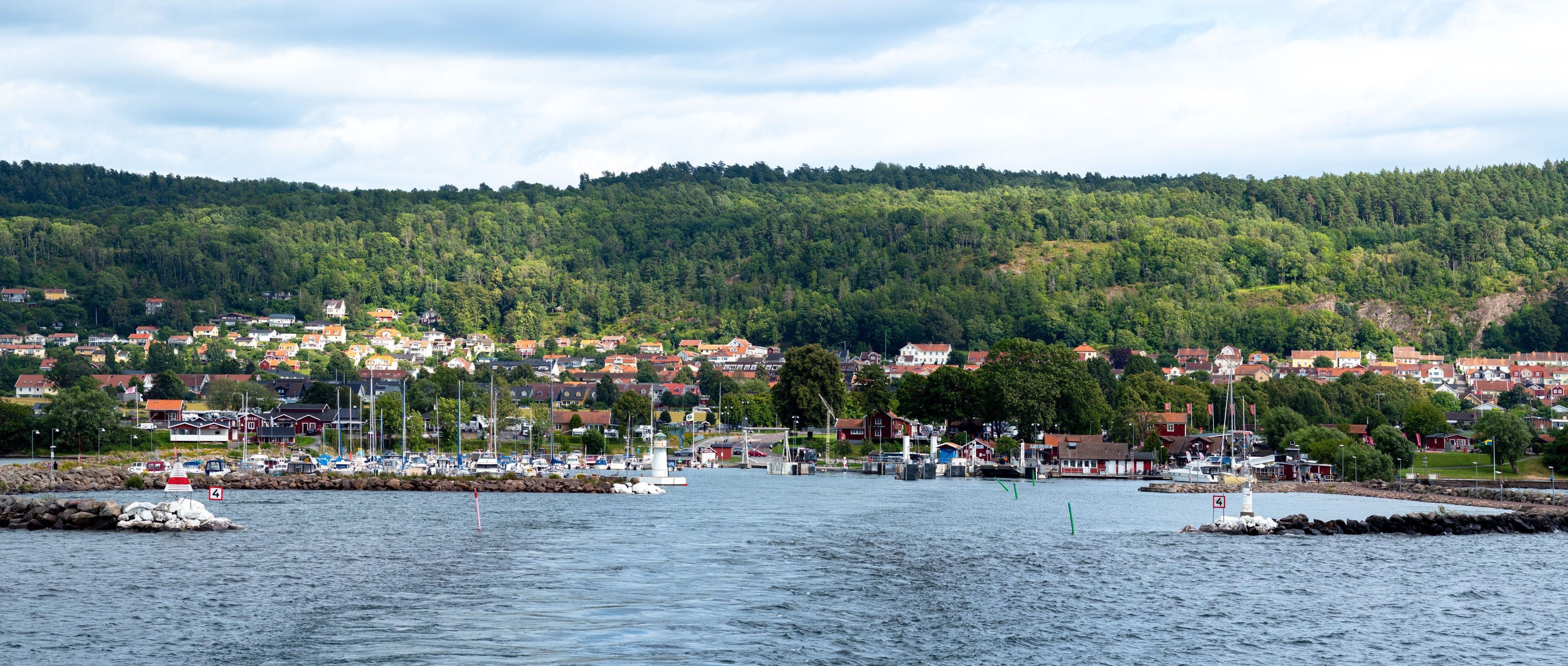 Gränna hamn med Grännaberget i bakgrunden sett från vattnet. Solen lyser upp landskapet fläckvis genom molnen.