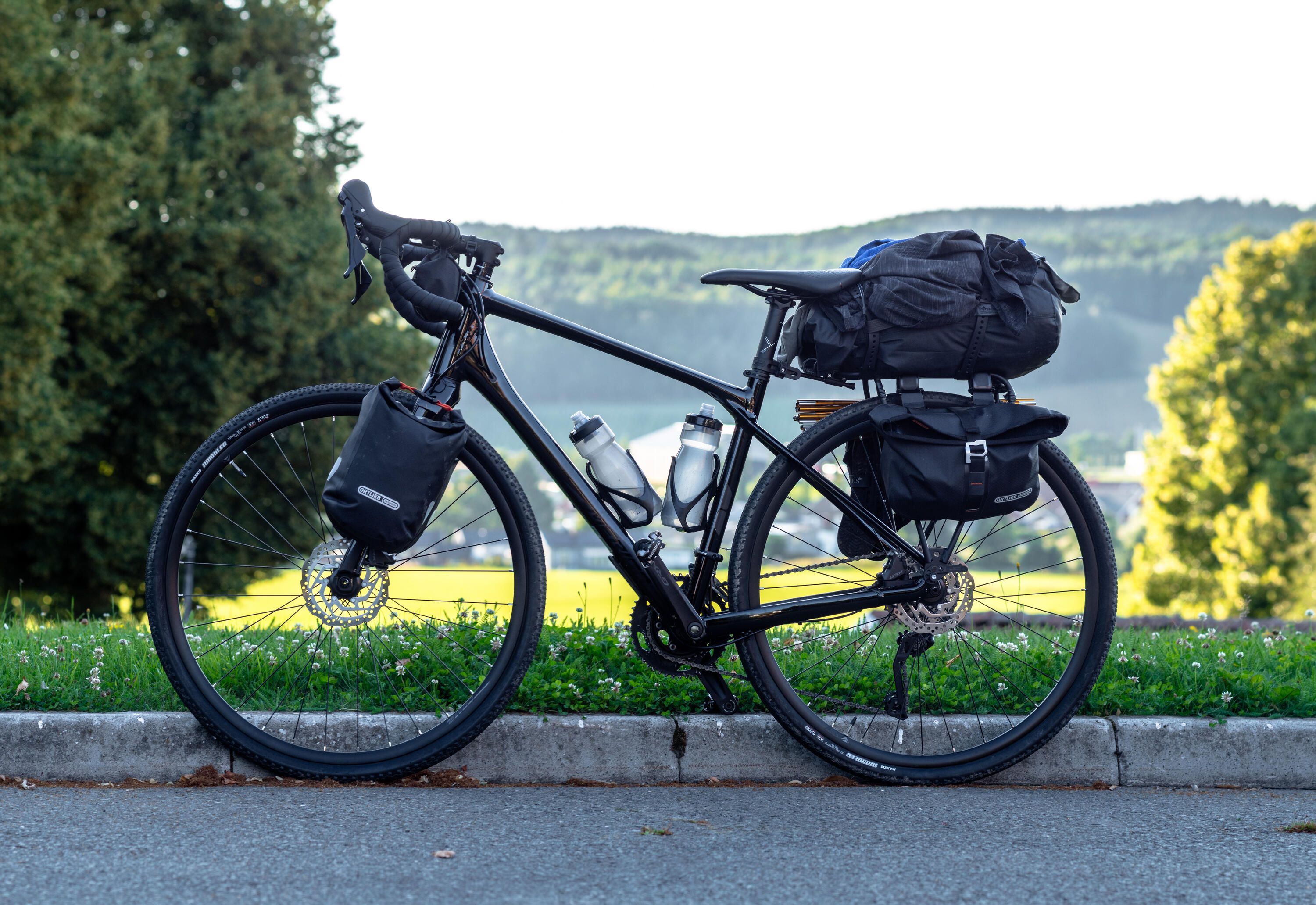 En svart cykel med väskor monterat på framgaffeln, styret samt baktill på en pakethållare. I ramen sitter det två vattenflaskor. På sidan av pakethållaren är tältpinnar, en sidoväska och ett par skor fästa. Cykeln syns i profil.