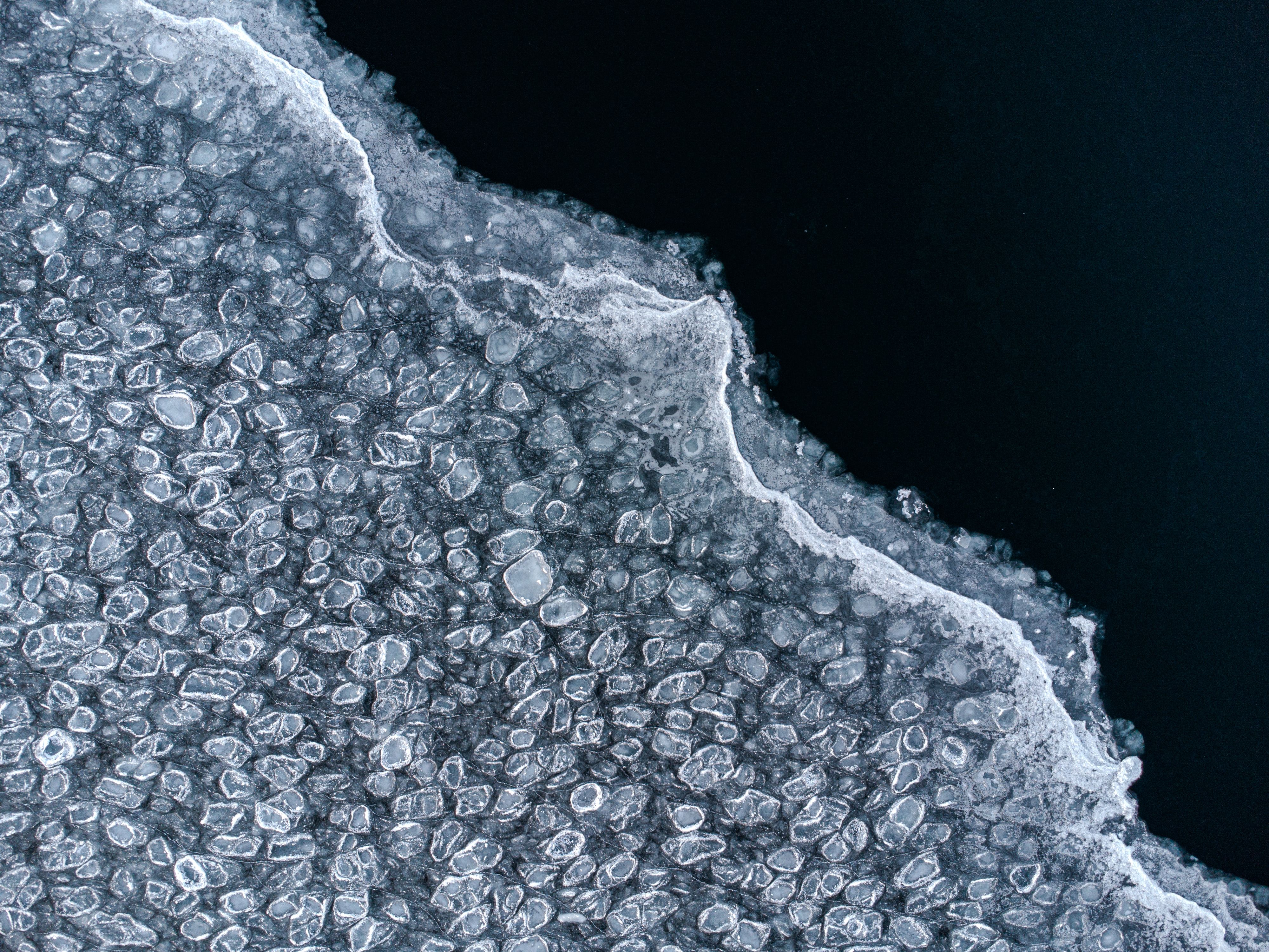 Is på en sjö sett uppifrån. Till vänster i bilden är äldre is som har frusit i många små cirklar. Till höger i bilden är ny, tunnare is som är helt transparent och det enda som syns är det mörka vattnet. Övergången mellan de två isarna delar bilden diagonalt.