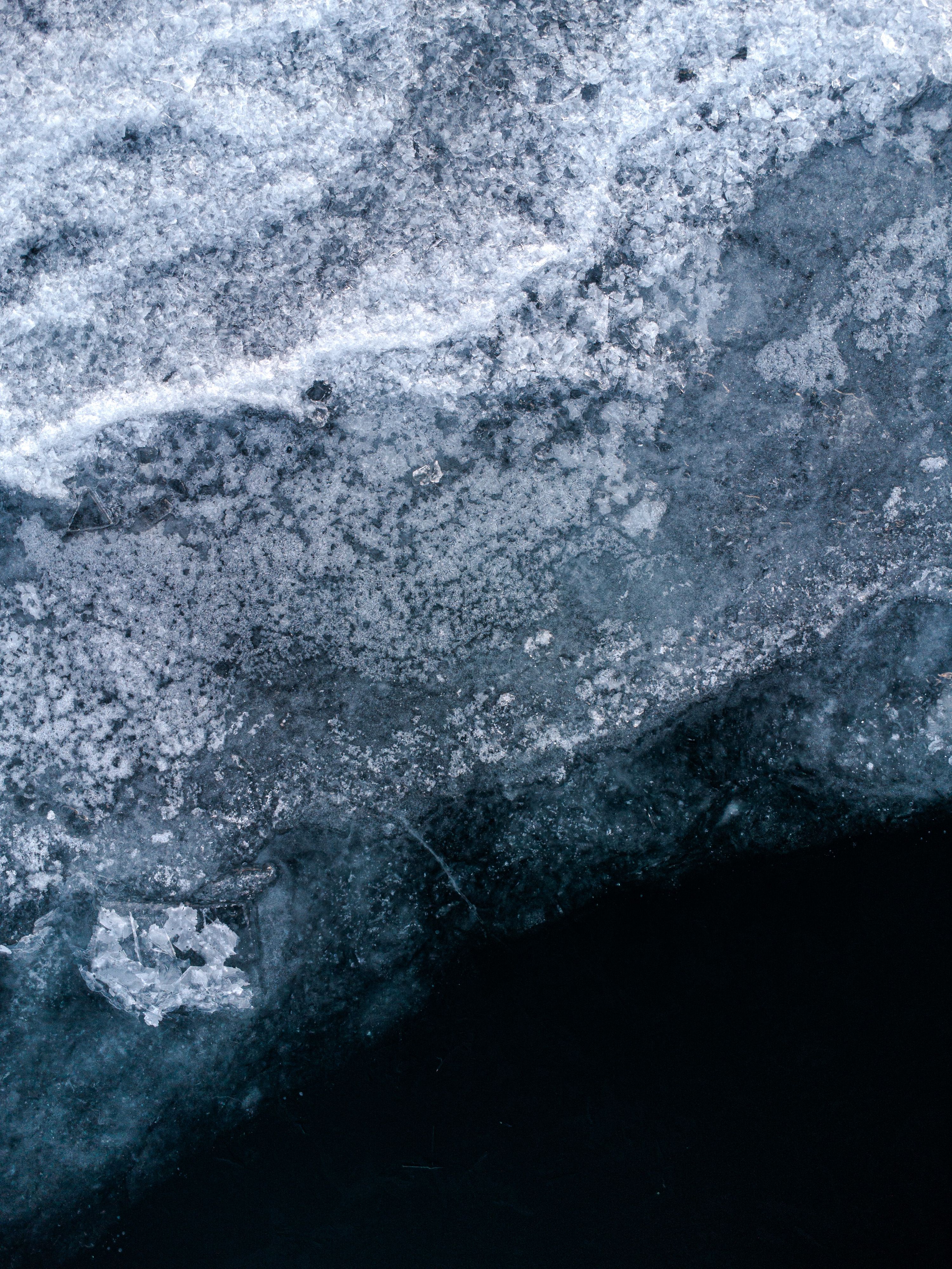 Is på en sjö sett uppifrån. Längst upp i  bilden är äldre is som är nästan helt vit och inte går att se igenom. Längst ner i bilden är ny, tunnare is som är helt transparent och det enda som syns är det mörka vattnet. Övergången mellan de två isarna delar bilden diagonalt.