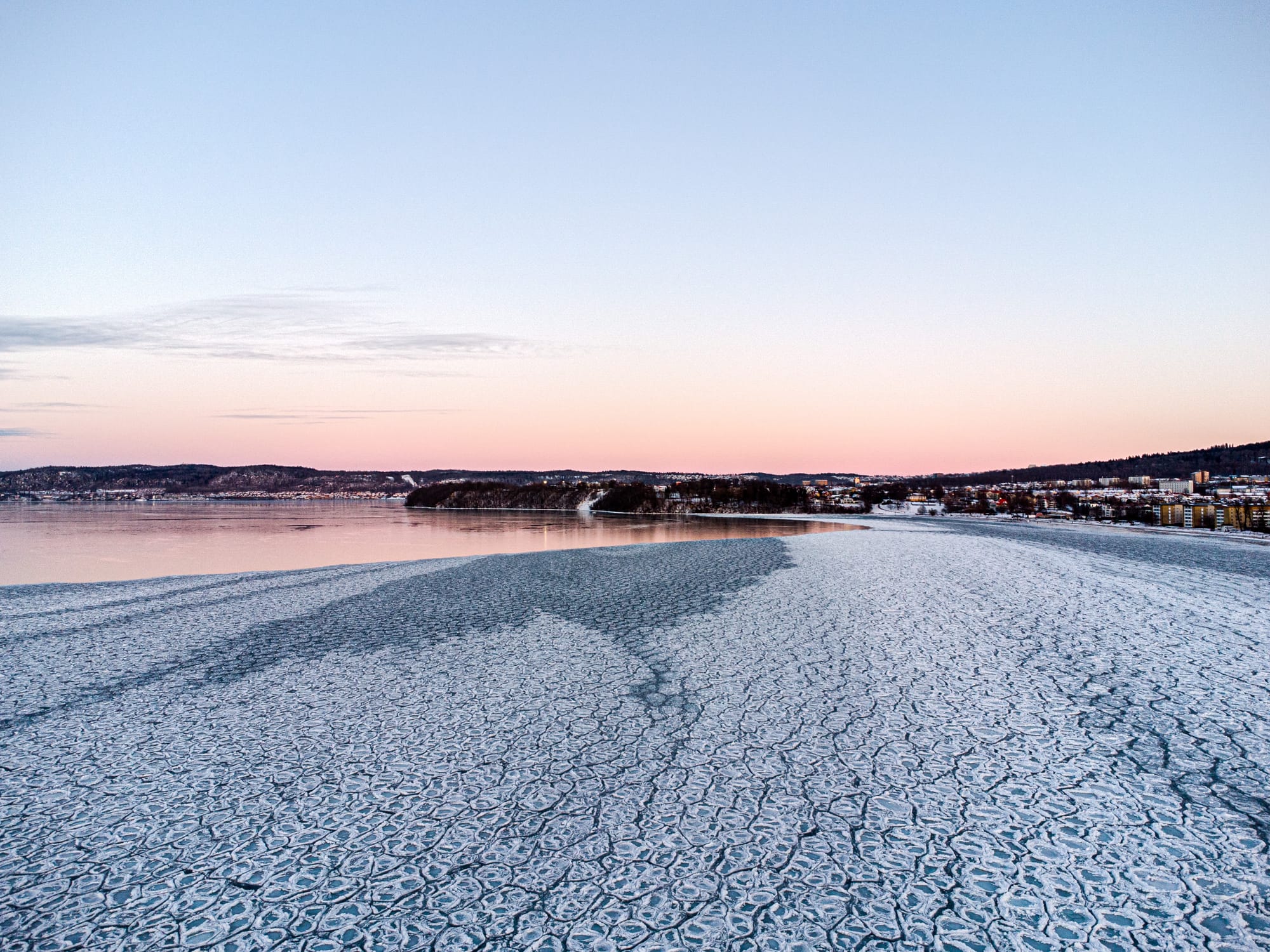 Frusen is längs med Vätterstranden med Rosenlunds bankar i bakgrunde. Isen till höger i bild intill stranden har frusit i ett mönster av en massa celler. Isen till höger utanför är frusen till en nästan perfekt blank is.