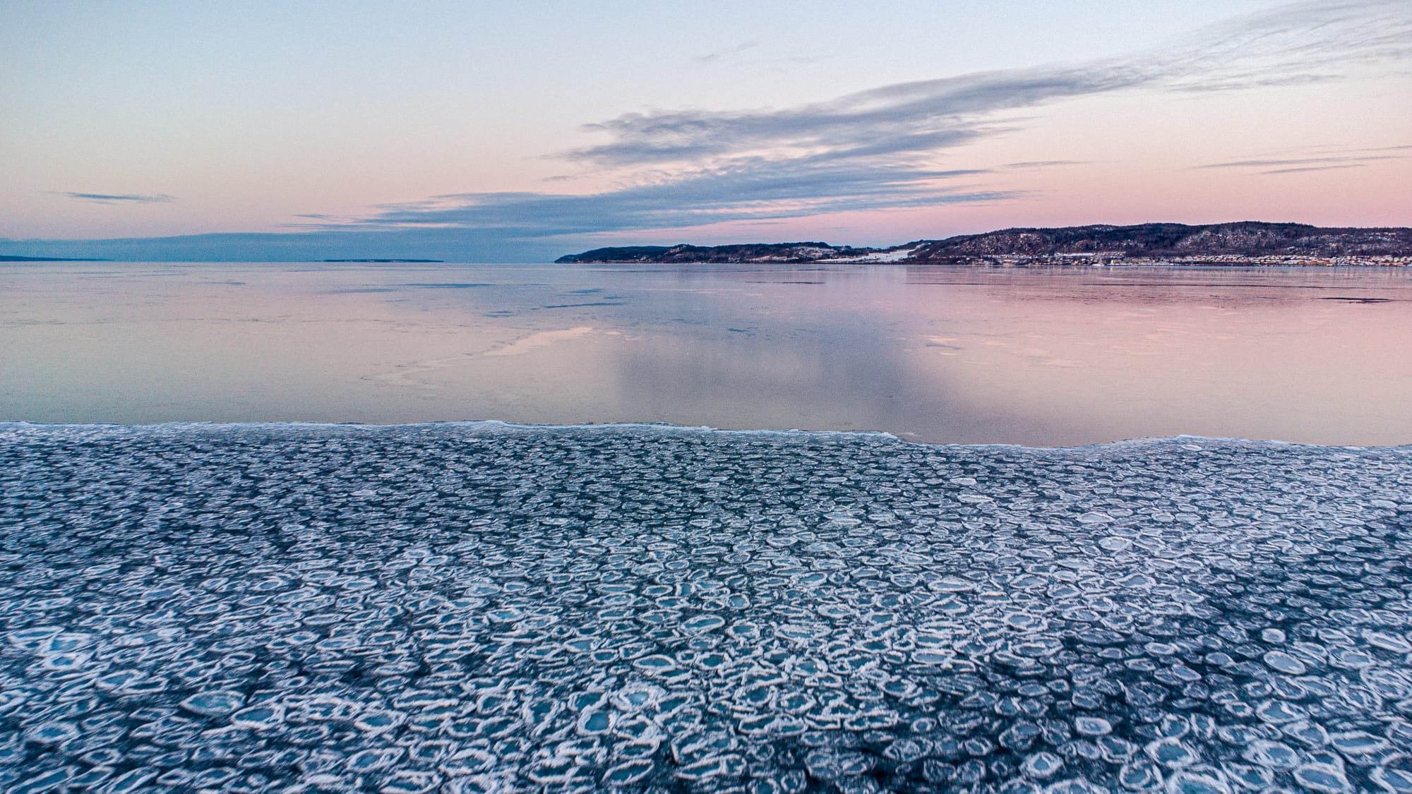 Vättern med Vista kulle och Visingsö borta i horisonten. I förgrunden syns is som frusit i ett mönster av celler. Vid en viss linje bryts mönstret tvärt och övergår i nästan fin blank is.
