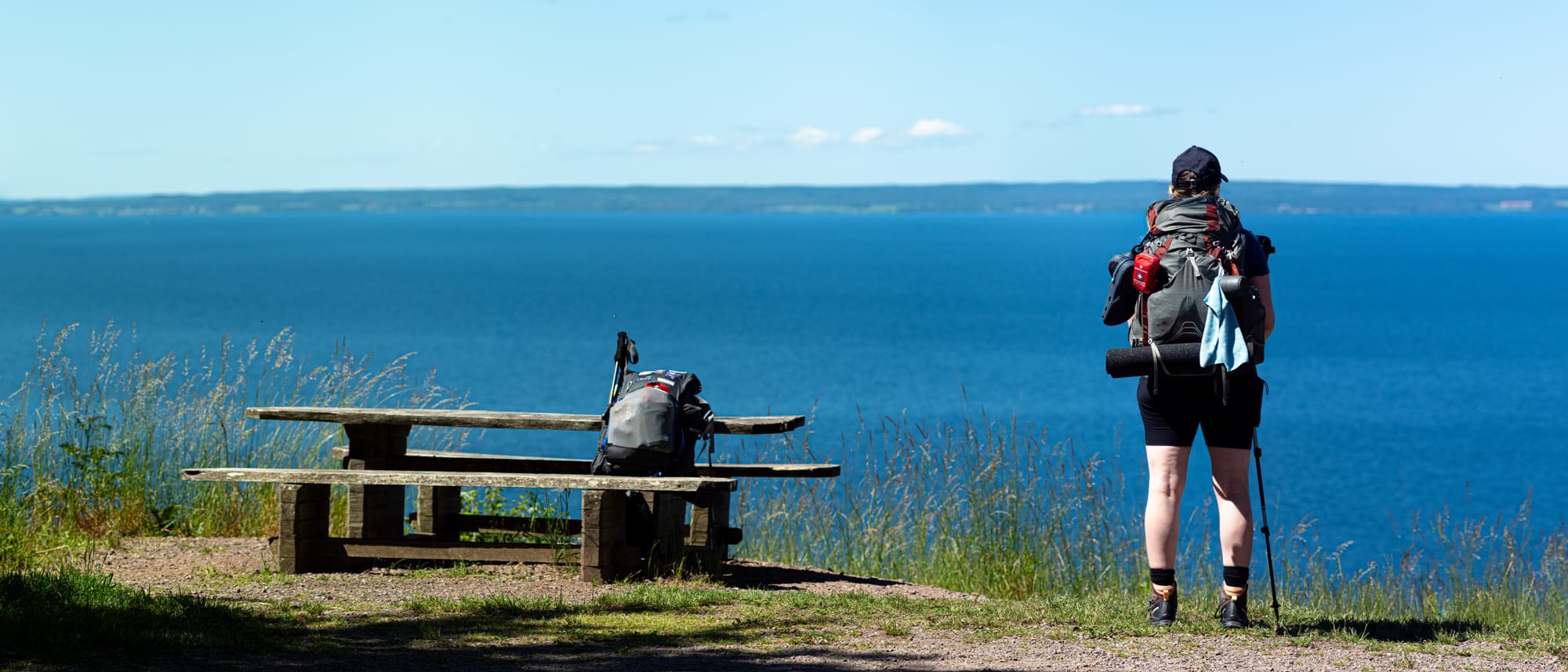 En person som står bredvid ett picknickbord och tittar ut över en stor blå sjö.
