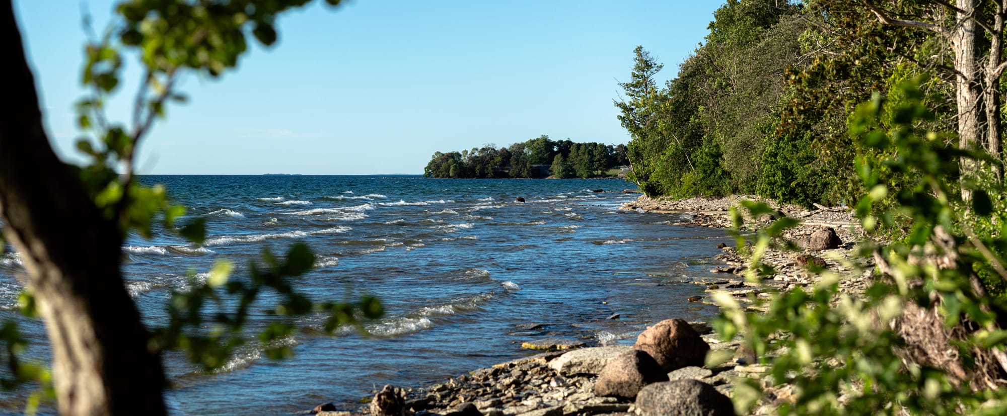 En stenstrand som det slår in vågor över. Stranden är bara några meter i djup och sedan börjar skogen.