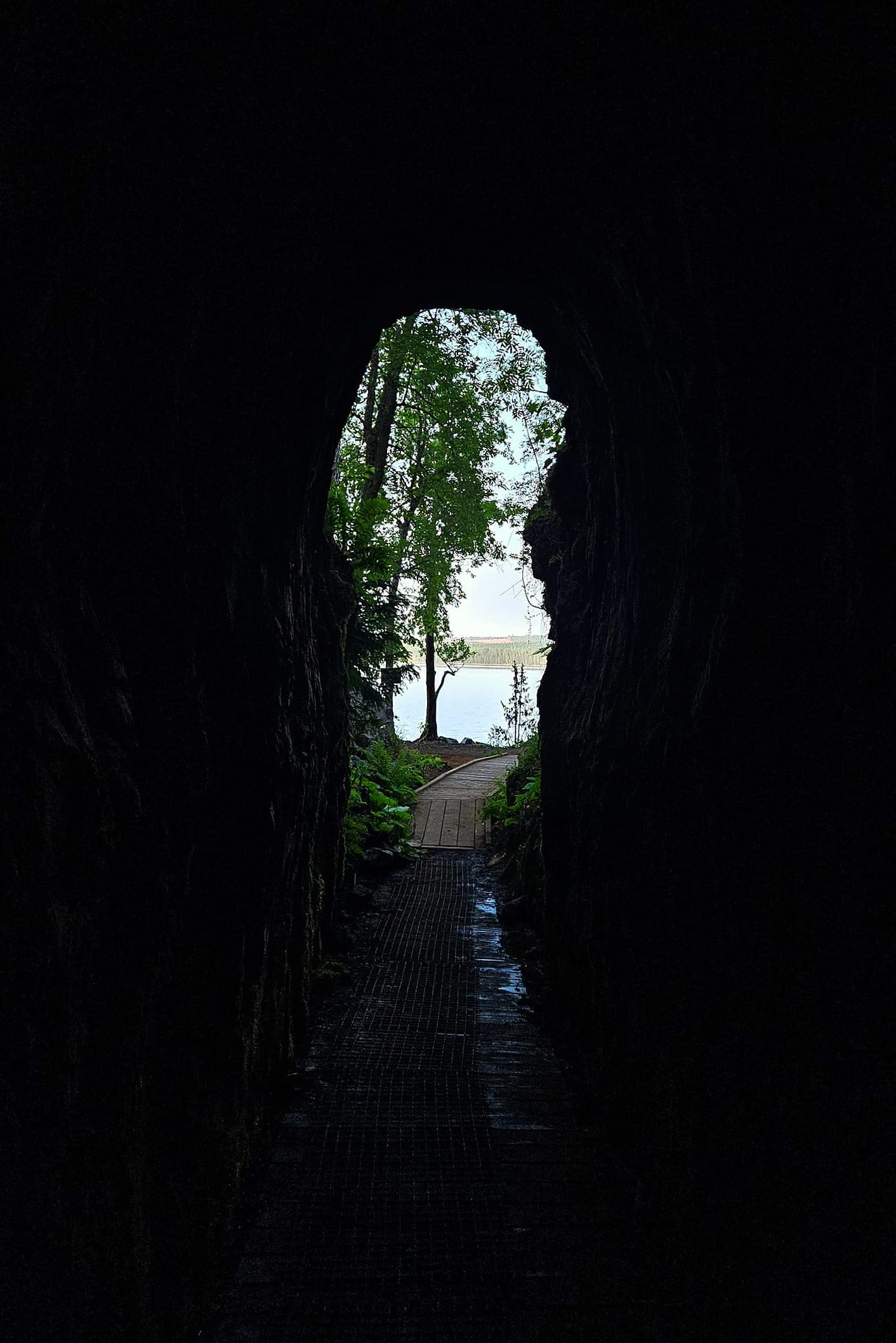 En vy från en mörk gång mot mynningen där en trägång syns med en sjö i bakgrunden.