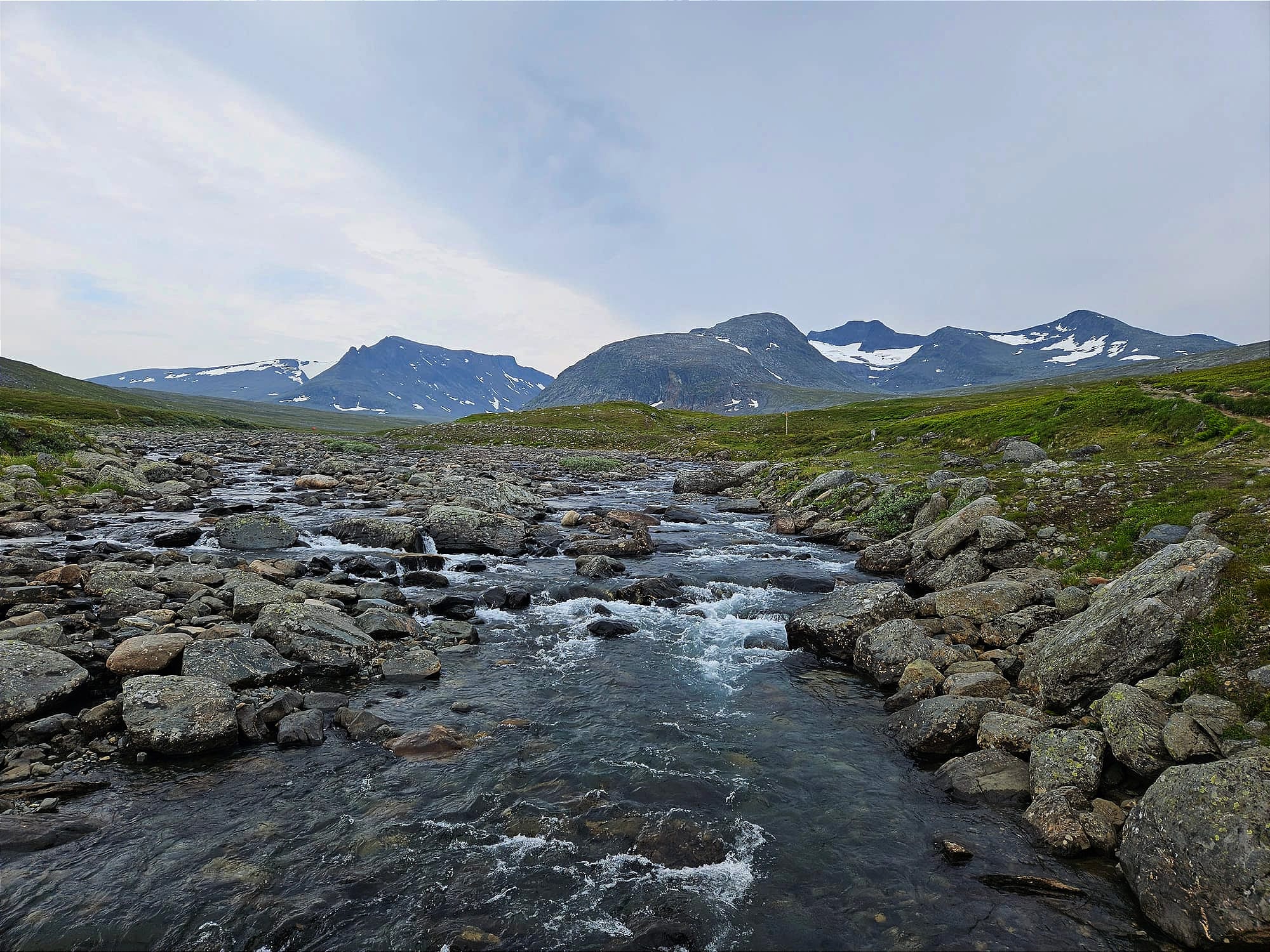 En stenig bäck med en bergskedja i bakgrunden under en molnig himmel
