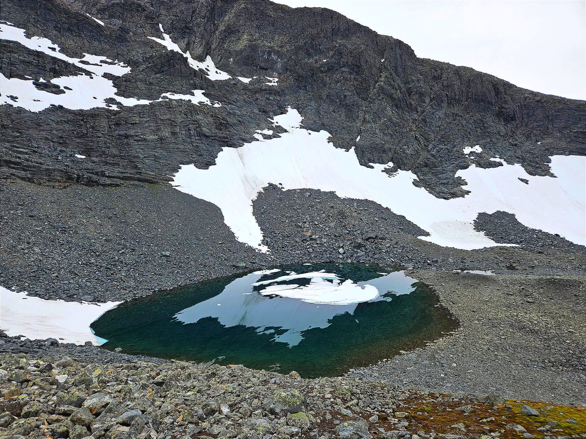 En blågrön sjö med flytande isflak på i foten på ett brant berg.