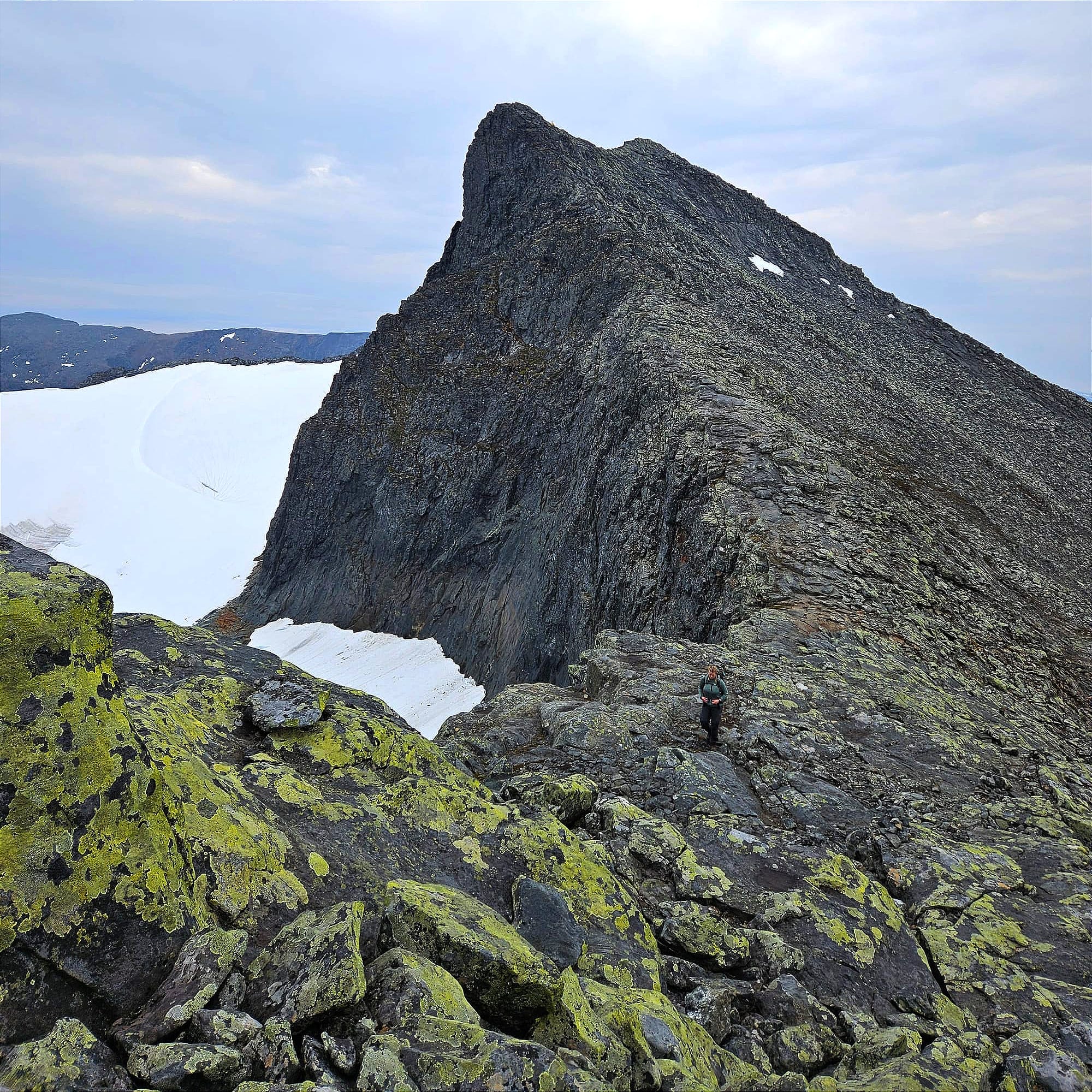 En person på väg upp för en liten bergstopp med en hög brant bergstopp i bakgrunden.