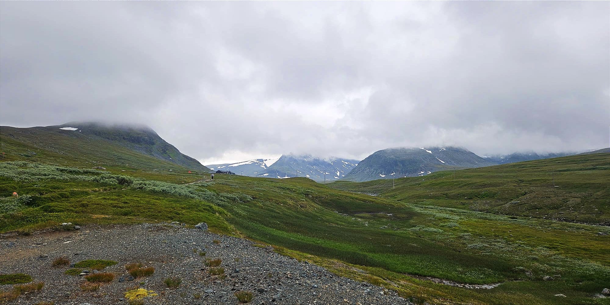 En dal täckt av låga moln som bildar ett tak. Dalen har höga alpina berg på sidorna och är täckt av kalfjällsgrönska.
