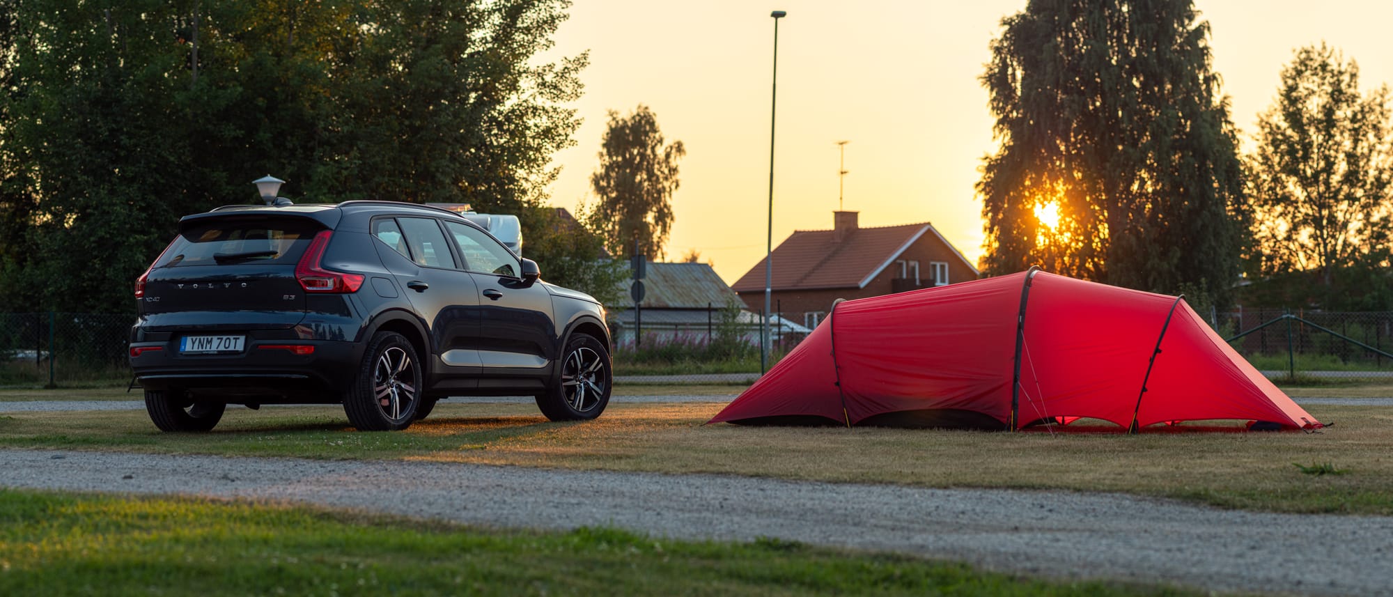 En mörkblå bil intill ett uppslaget rött tunneltält på en camping
