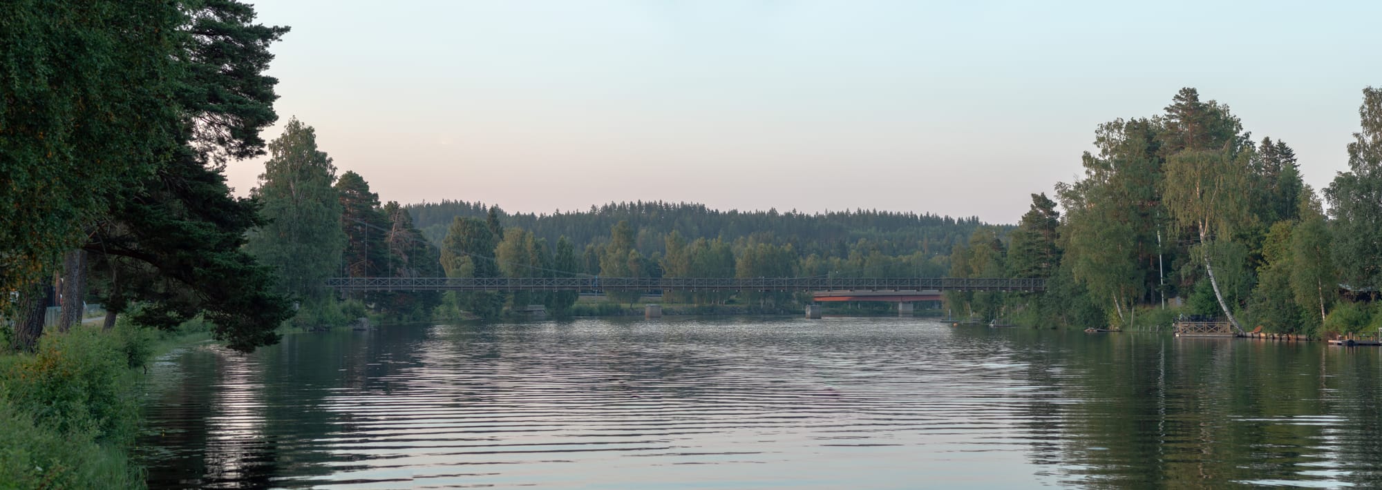 En stilla å på kvällen med två broar som går över. Båda strandkanterna är täckta av träd med några bryggor