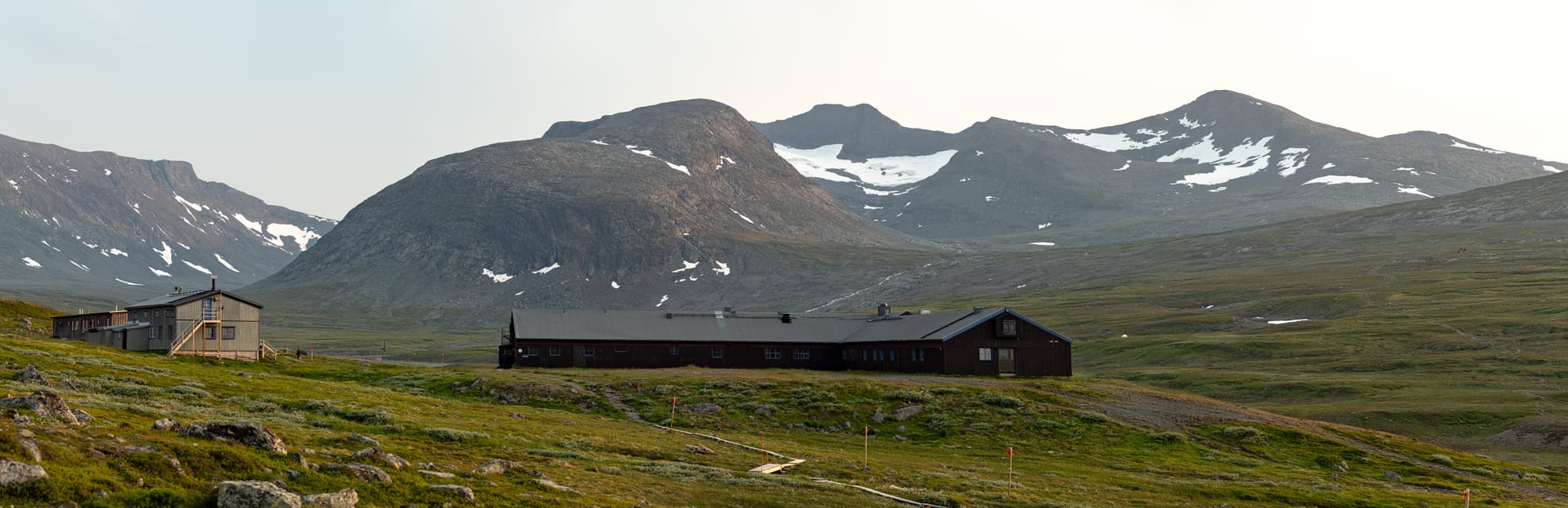 Flera byggnader vid foten av en stor bergskedja med glaciärer i kvällssolen.
