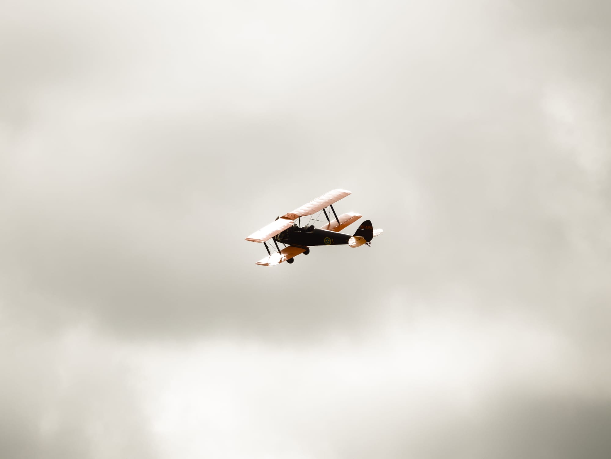Ett orangefärgat gammalt dubbelvingat flygplan mot en molnig himmel