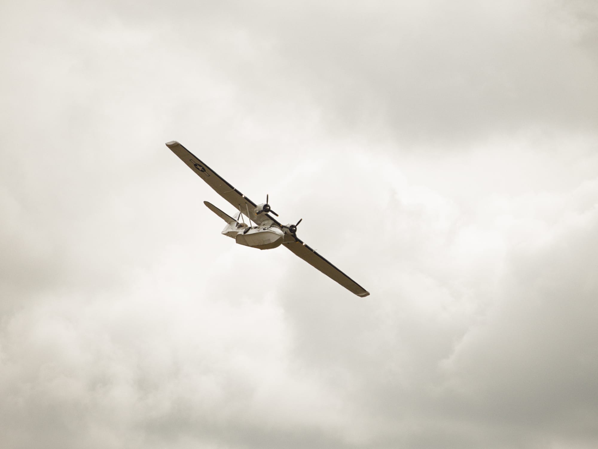 Ett gammalt propellerflygplan mot en grå himmel. Flygplanet har en kropp som gör det möjligt att landa på vatten.