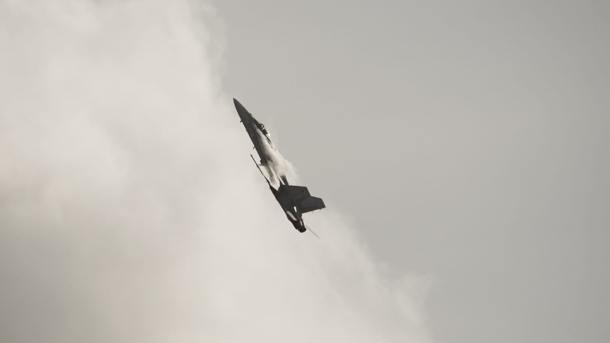 Ett stridsflygplan mitt i en manöver för att svänga rakt upp. Det är jetstrimmor som bildats på ovansidan av vingarna.