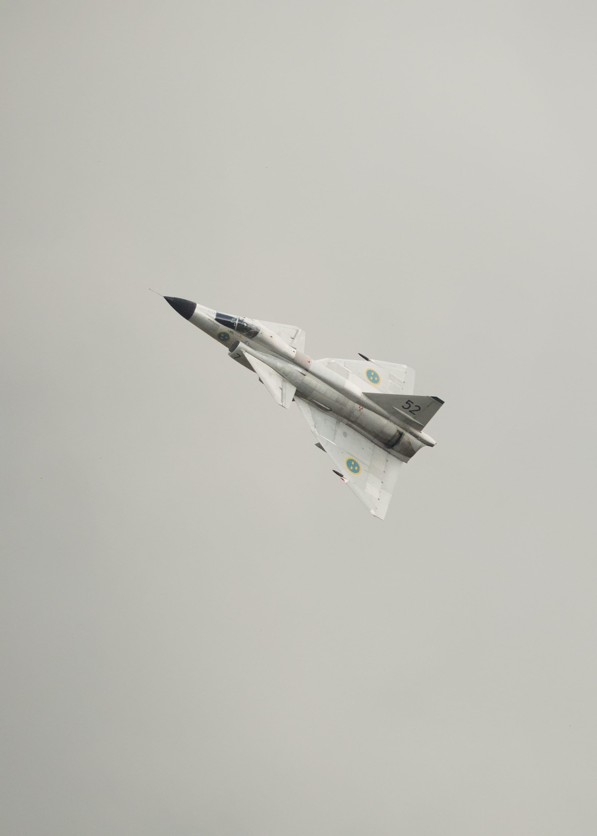 Ett grått stridsflygplan med canardvingar som visar sin ovansida och med solen som lyser uppifrån. På vingarna syns skölden för det svenska flygvapnet med tre kronor.