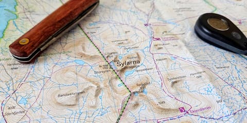 En karta över Sylarnamassivet sedd snett från sidan. På kartan ligger en fällkniv och en termometer.