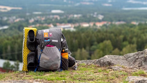 En fullastad ryggsäck som står på en höjd. I bakgrunden syns en dal med ett samhälle i skogen.